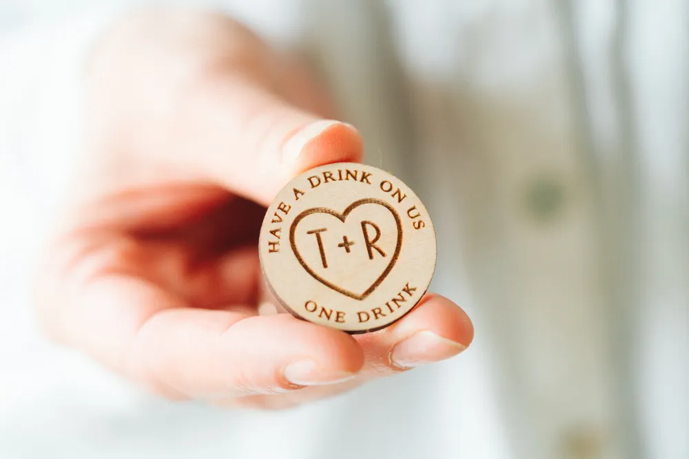 Personalised wooden wedding drink tokens with engraved design displayed in a pile on wooden surface