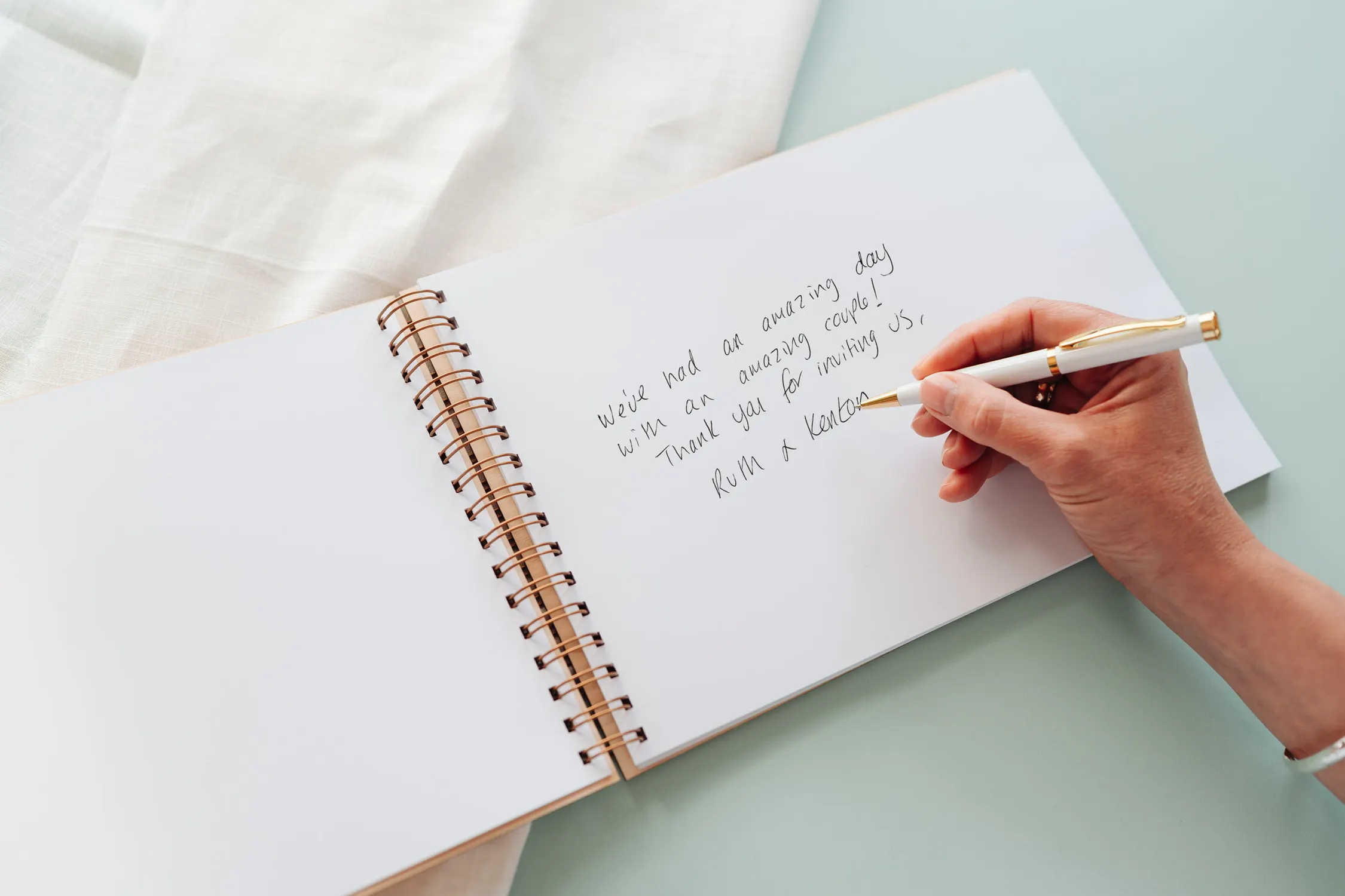 Open spiral-bound wooden wedding guest book showing Instax mini photos and guest messages on thick 160gsm white pages
