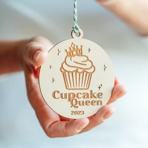 Home 11 Hand holding an engraved wooden Cupcake Queen Christmas bauble with a crowned cupcake and green and white string