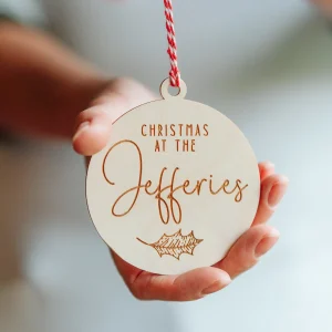 Home 15 Personalised wooden family Christmas bauble engraved 'Christmas at the Jefferies' with a holly leaf, held in a hand