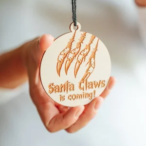 Home 9 Hand holding a wooden Santa Claws is coming horror Christmas bauble with claw marks and black string