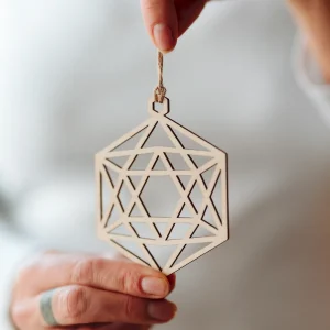 Home 7 Hand holding a laser-cut wooden geometric hexagon Christmas bauble on natural yarn