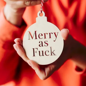 Home 3 Hand holding a cut-out wooden Merry as Fuck rude Christmas bauble against a red jumper