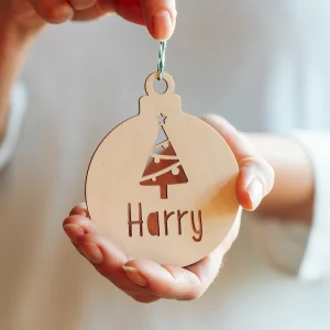 Home 13 Wooden personalised name Christmas bauble with cut-out Christmas tree and the name Harry, held in a hand